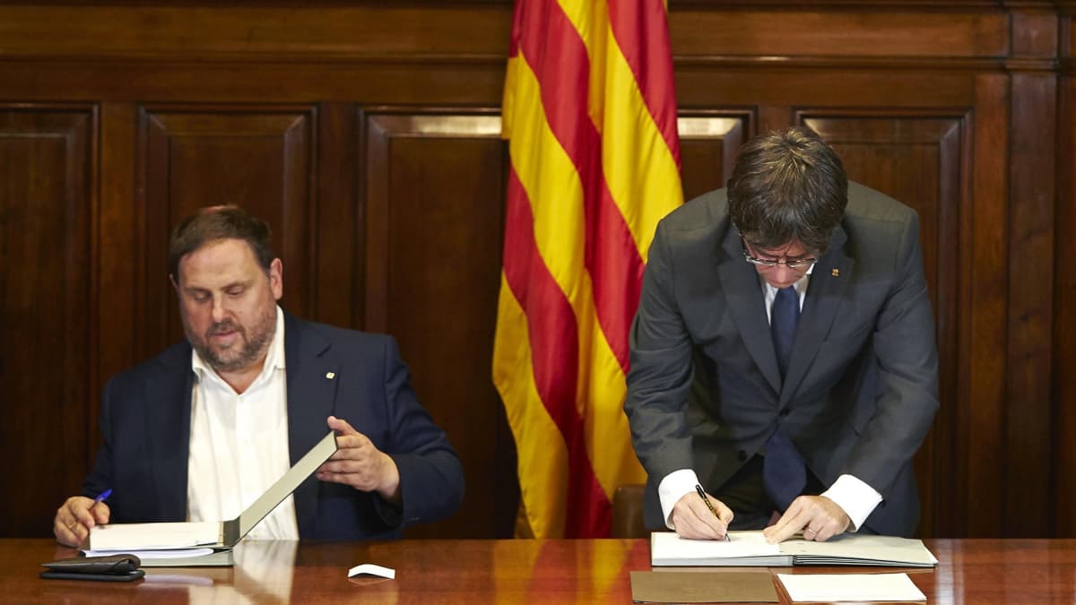Katalonian aluehallinnon johtaja Carles Puigdemont (oik.) allekirjoittamassa asetusta itsenäisyyskansanäänestyksestä. Vieressä istuu aluehallinnon varajohtaja Oriol Junqueras.