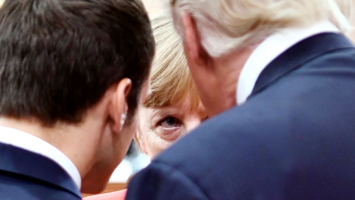 Angela Merkelin silmä näkyy miesten välistä.