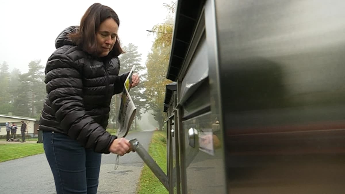 Nainen toppatakissa avaa avaimella postilaatikkoa