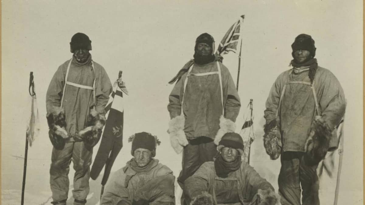 Kellertävä valokuva viidestä 1900-luvun alun retkivaatteisiin pukeutuneesta, pakkasen puremasta miehestä lumihangessa.