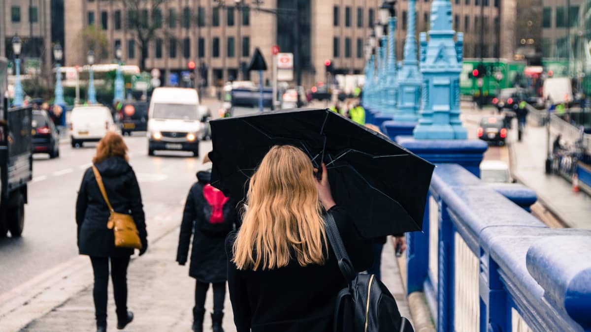 Nainen kuvattuna Lontoon kadulla sateenvarjo kädessään.
