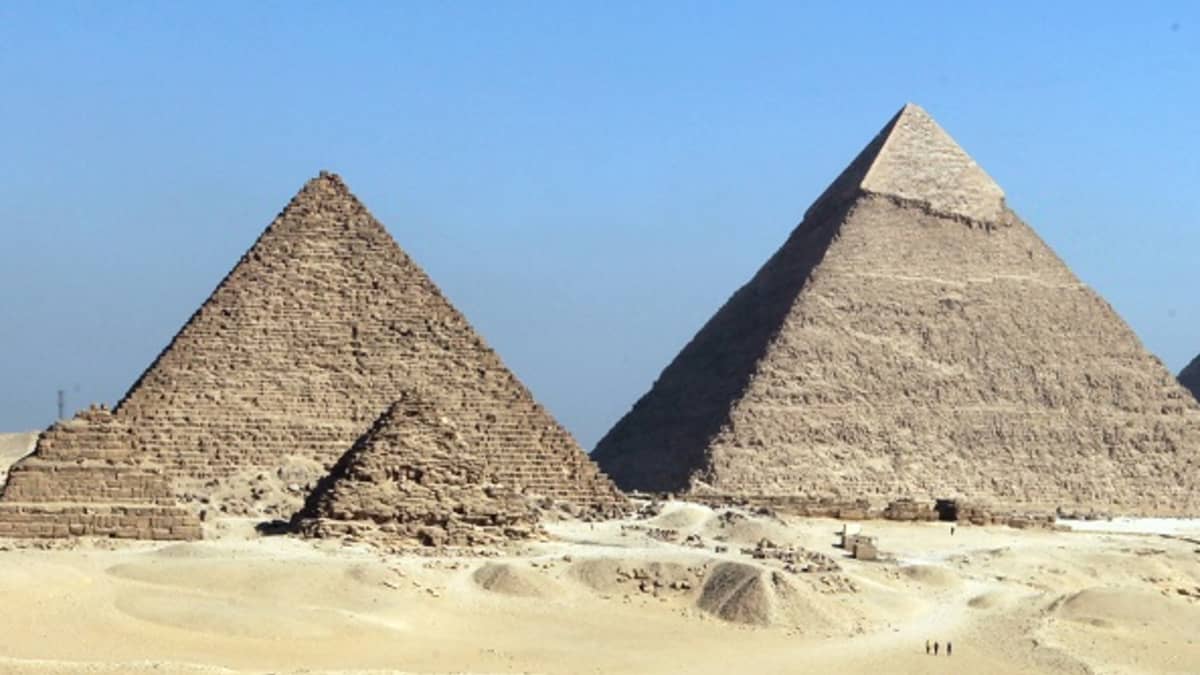 Kolme isoa ja kolme pientä pyramidia hiekka-aavikolla.