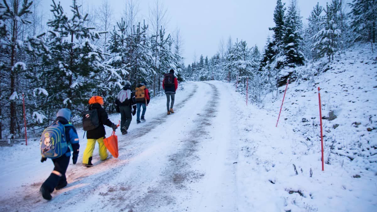 Lapsia kulkee tietä pitkin metsässä talvella.