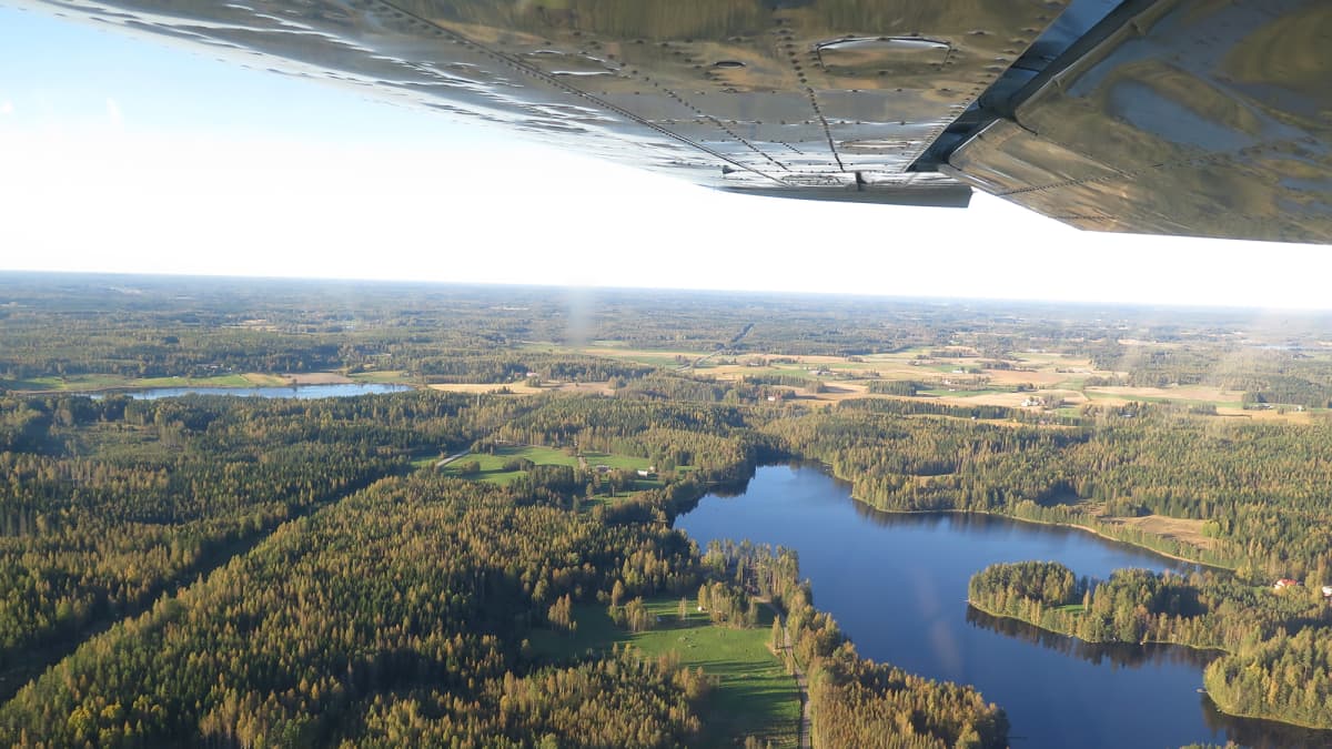 Järvi- ja metsämaisemaa ilmasta kuvattuna, ylälaidassa lentokoneen siipi.