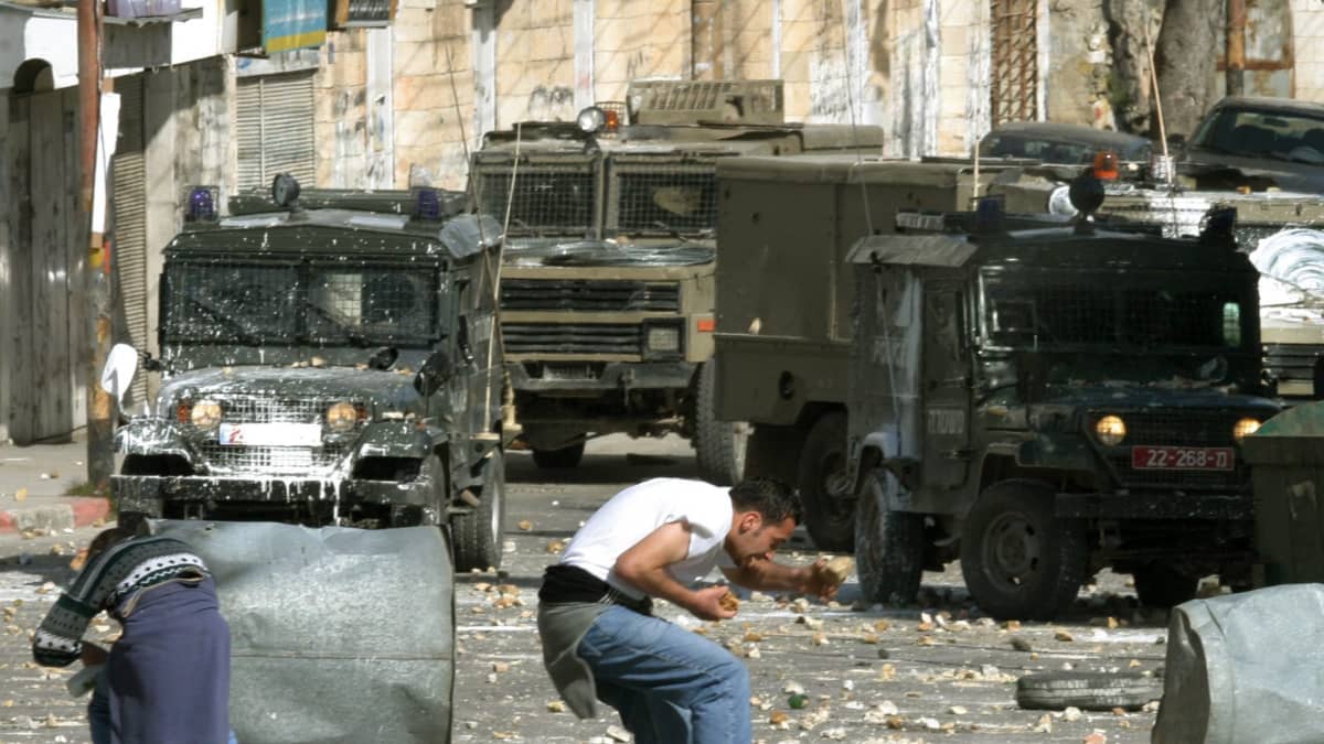 Palestiinalaiset nuoret miehet osoittavat mieltään ja heittivät kiviä israelilaisia ajoneuvoja kohti tammikuussa 2004. 