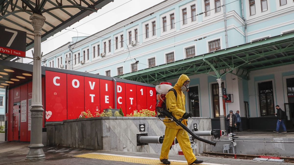 Työntekijä puhdistaa suojapuvussa juna-asemalla sijaitsevaa korona-testipaikan edustaa.