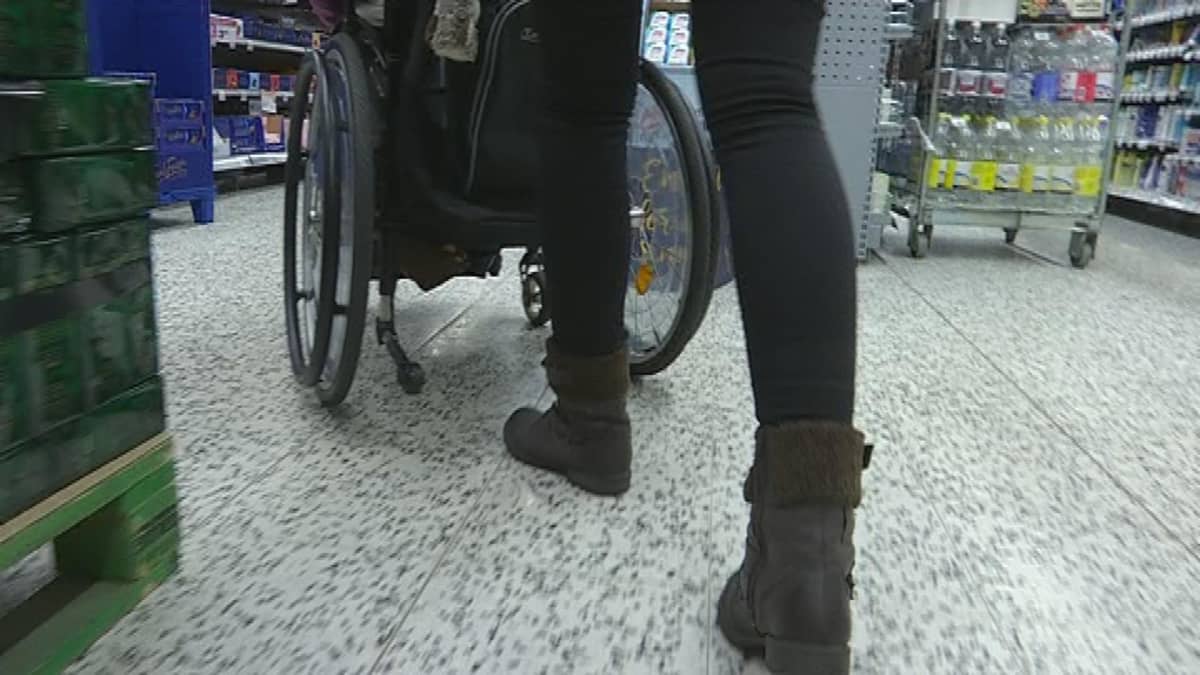Henkilöhtainen avustaja työntää avustettavan pyörätuolia kaupassa.
