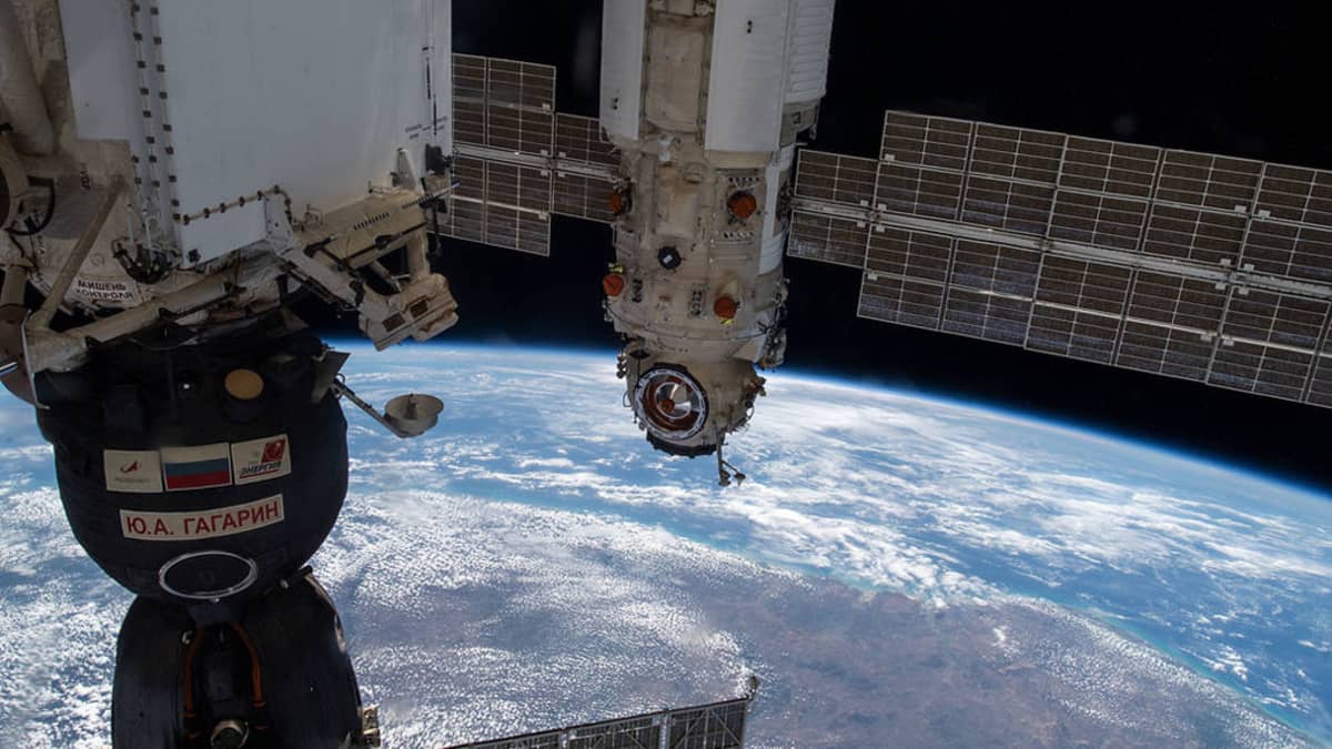 ISS:n moduleja ja osa Sojuz-aluksesta, alla maapallon kaareva pinta pilvien täplittämänä. 