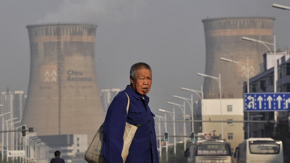 Vanha kiinalaismies kävelee kadulla ruokaostoksia kantaen. Taustalla kohoaa suuri hiilivoimala. 