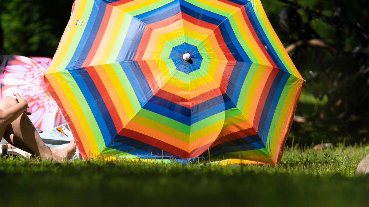 Sateenkaaren värinen päivänvarjo nurmikolla.