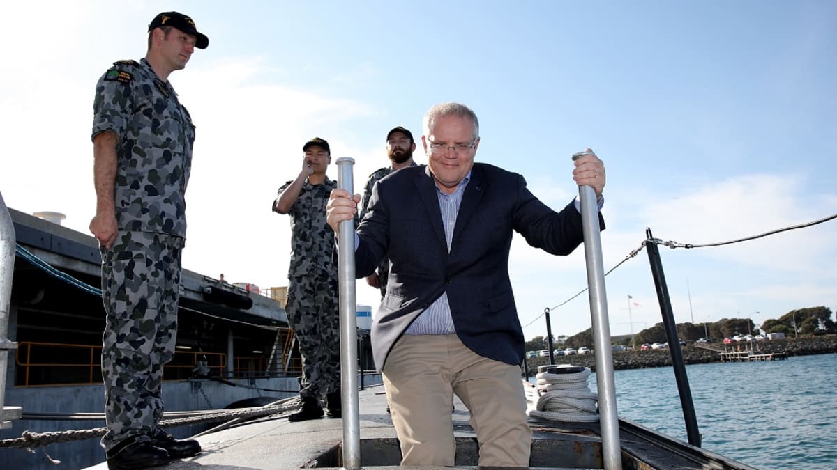 Kuvassa keskellä Australian pääministeri Scott Morrison menossa sukellusveneeseen. Hänen vasemmalla puolellaan seisoo yksi sotilas ja hänen takanaan kaksi sotilasta. 