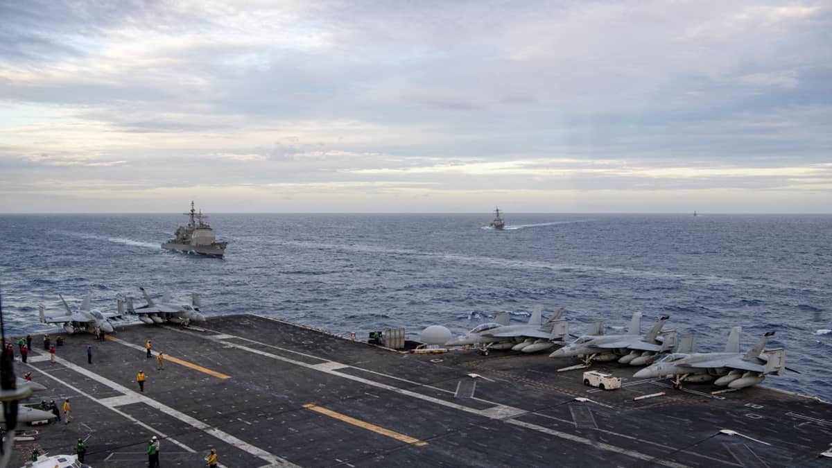 Kuvassa on Yhdysvaltojen lentotukialus, jonka takana näkyy kaksi sotalaivaa. 