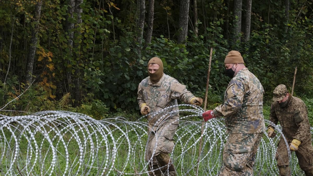 Kuvassa on kolme latvialaista sotilasta, jotka levittävät Valko-Venäjän rajalle piikkilanka-aitaa. 