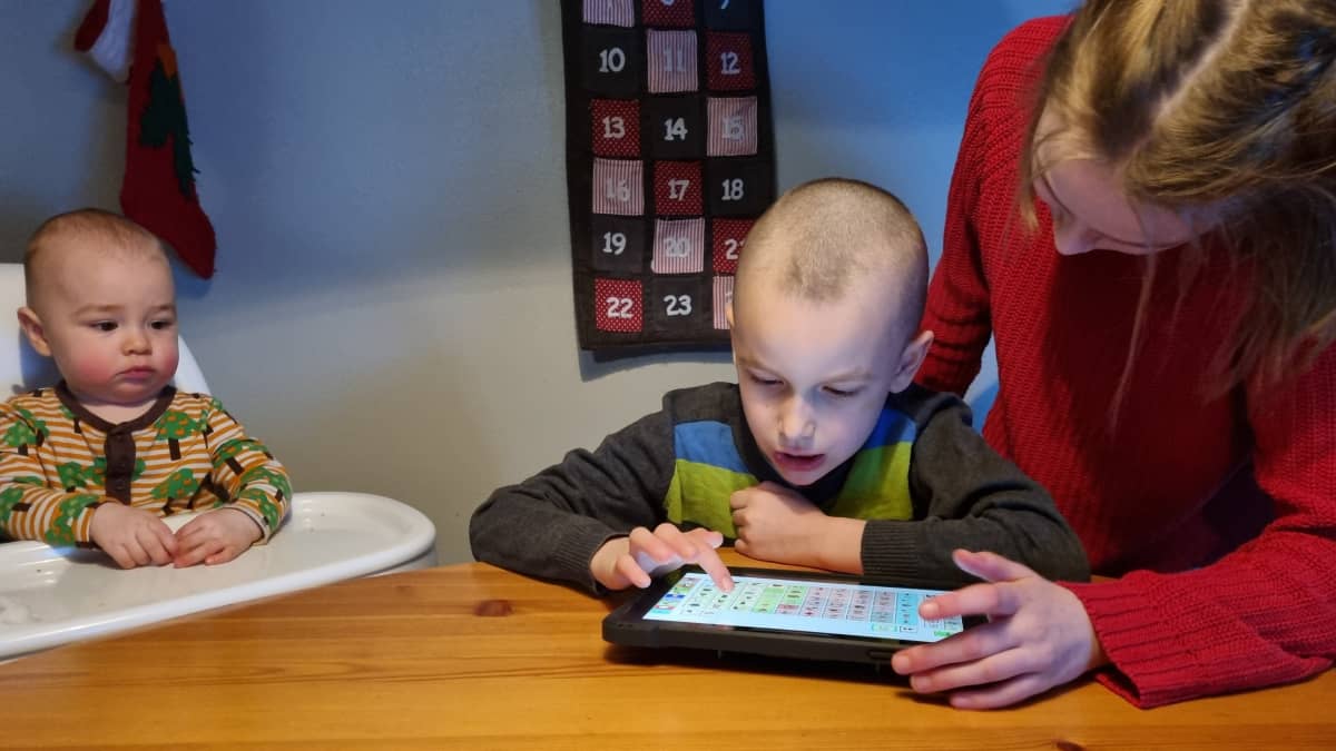 Collan-Karttusen perheen keskimmäinen lapsi käyttää keskustelun apuna kommunikaatiotablettia. Kuvassa ovat myös 1- ja 10-vuotiaat sisarukset.