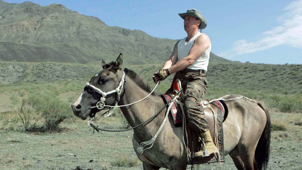 Hihattomaan paitaan, maastohousuihin ja stetsoniin pukeutunut Putin ratsastaa kallioisessa maisemassa. 