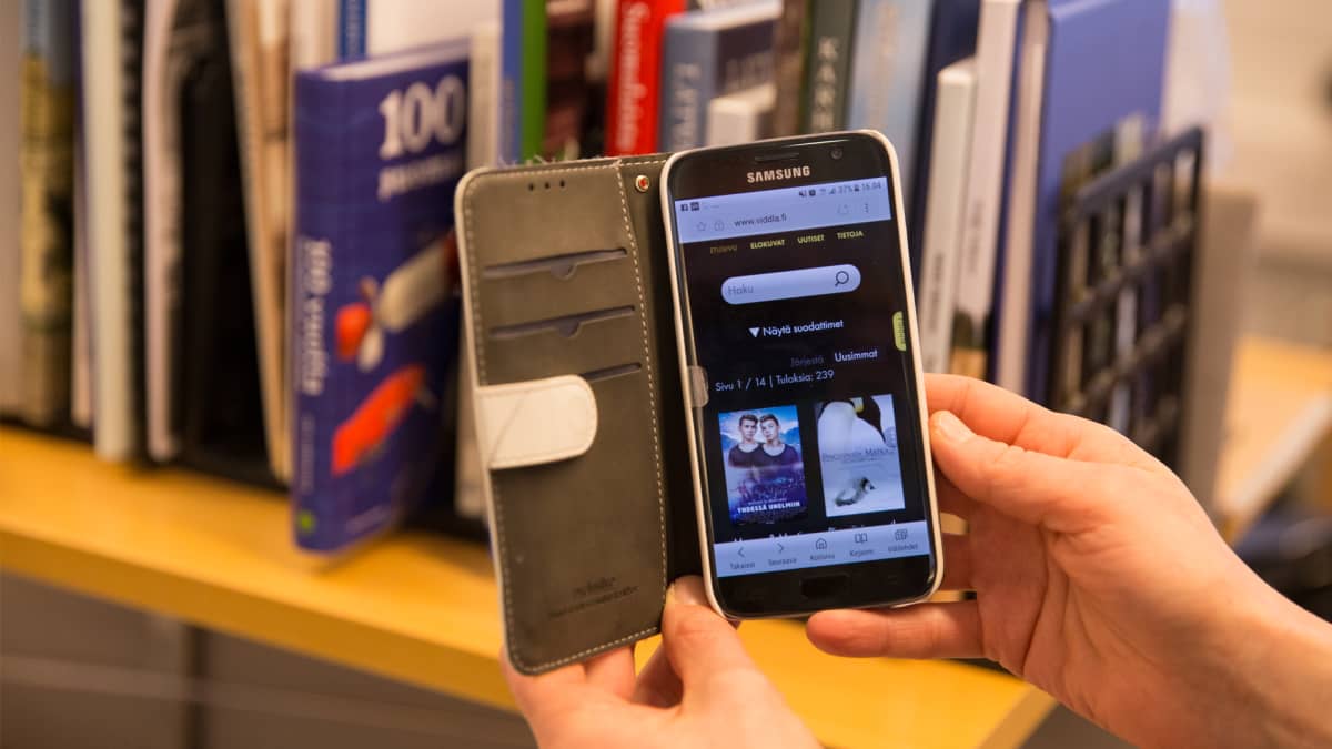 Kännykän käyttäjä selailee elokuvia kirjaston uudessa Viddla-palvelussa.