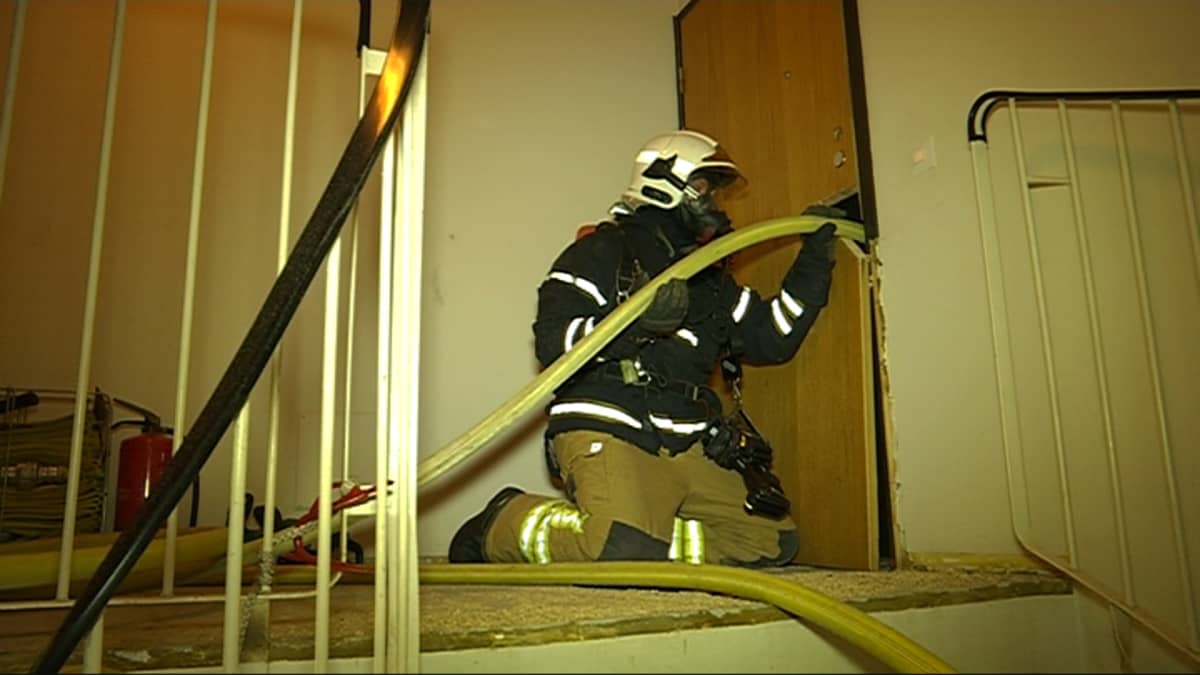 Palomies työntää vesiletkua kerrostaloasunnon oven läpi