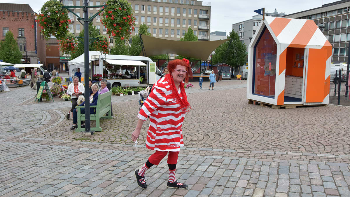 Punavalkoiseen asuun pukeutunut nainen kävelee Hämeenlinnan torilla
