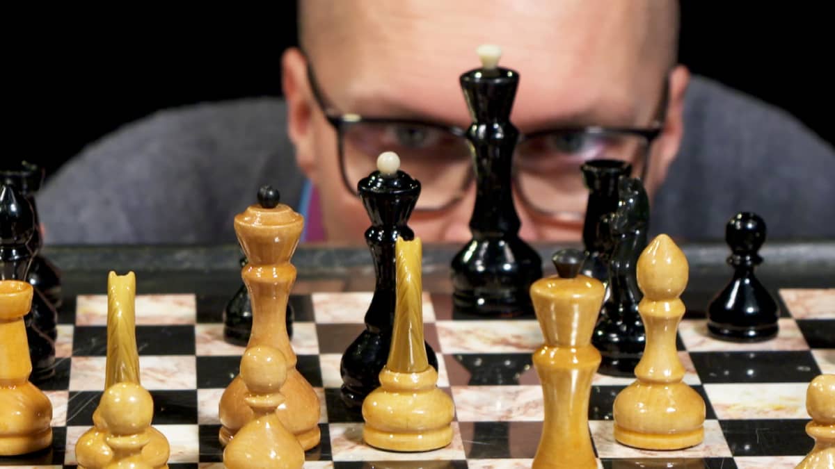 Mies katsoo shakkilautaa shakkinappuloiden takaa.