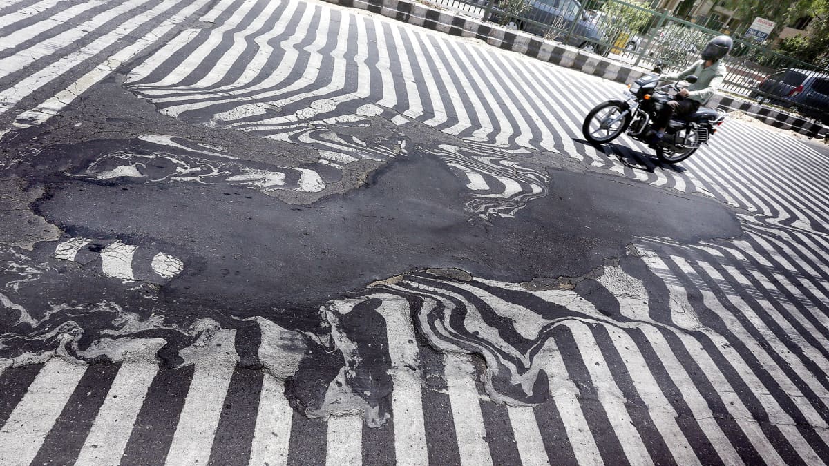 Mopedisti ajaa tiellä jossa osa valkoisesta viivoituksesta on sulanut kuumassa auringossa.