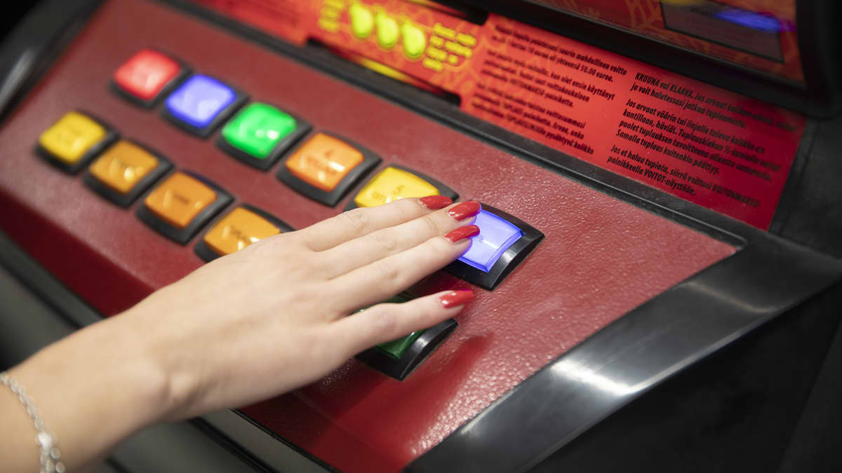 Rahapeliautomaatti lähikuvassa. Naisen käsi näppäimellä.