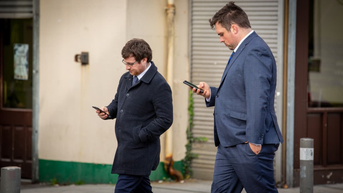 kaksi miestä kävelee kännykät kädessä