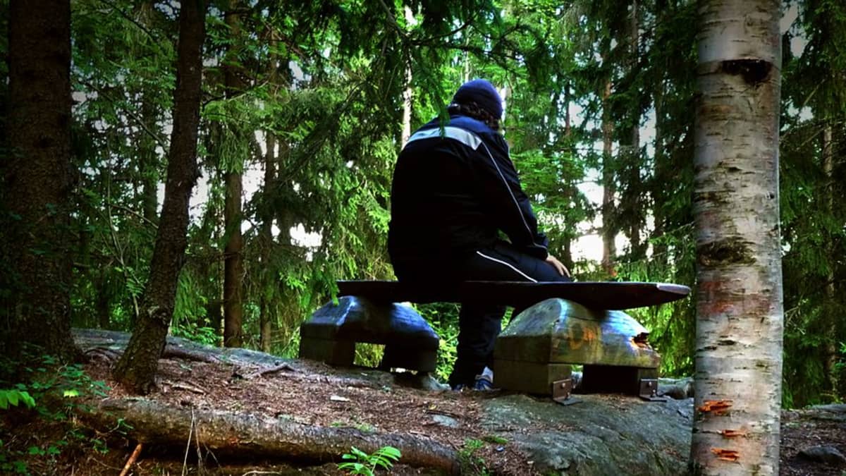 Mies istuu penkillä metsässä.