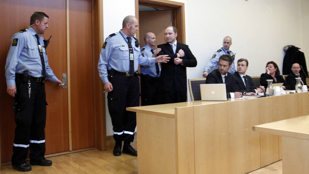 Anders Behring Breivik astuu oikeussaliin poliisisaattueessa.