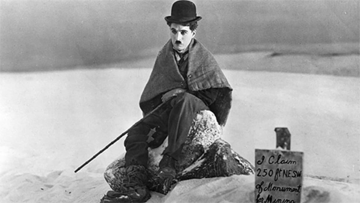 Charles Chaplinin kulkurihahmo istuu lumessa, vierassä kyltti kertoo hänen vallanneen maata kaivosta varten.