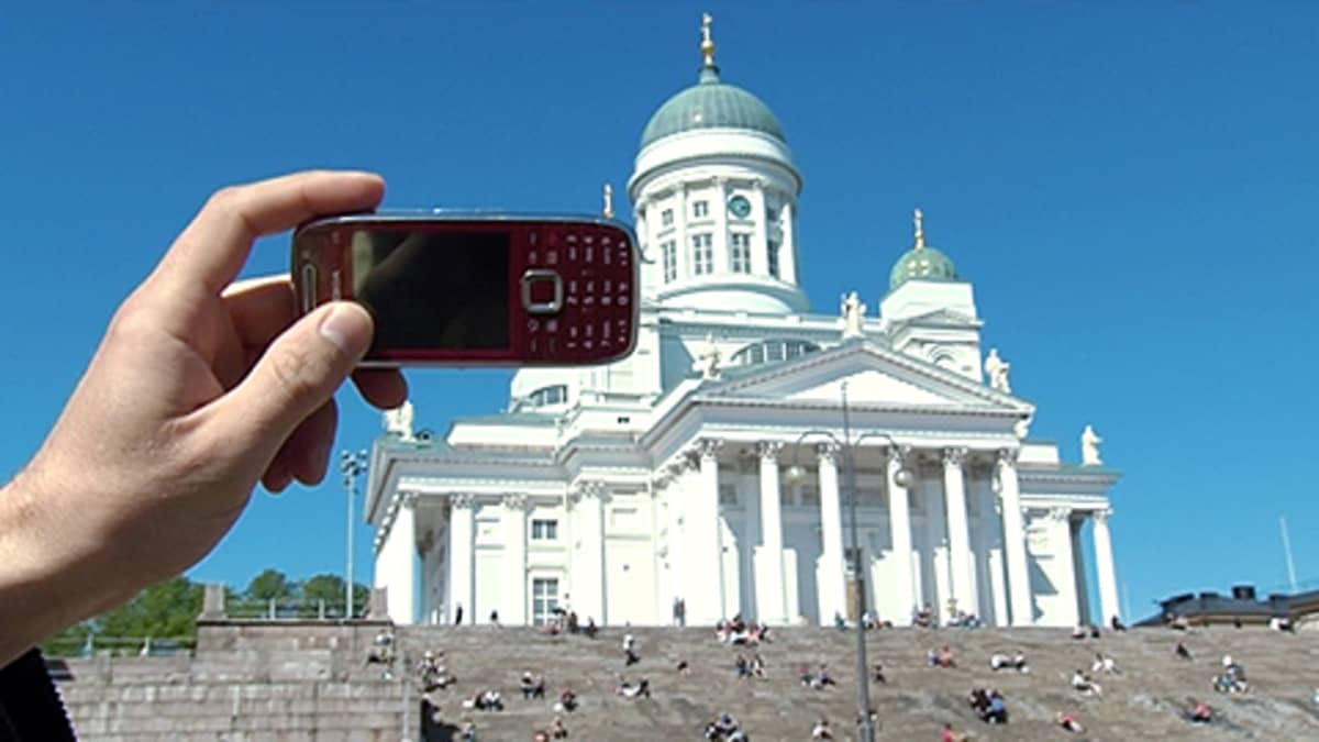 Miehen käsi pitää matkapuhelinta ottaakseen valokuvan Helsingin Tuomiokirkosta.