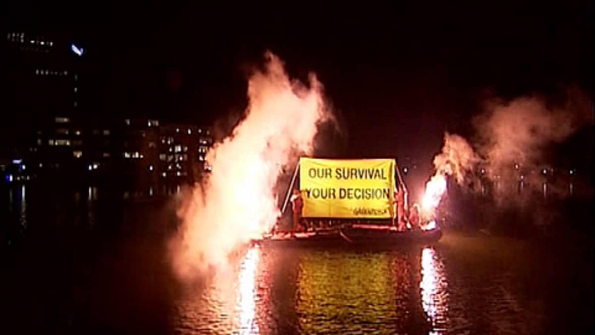 Greenpeacen edustajat sytyttävät soihtuja lautalla Kööpenhaminassa ja valaisevat julisteensa tekstin, jossa lukee "our survival, your decision".