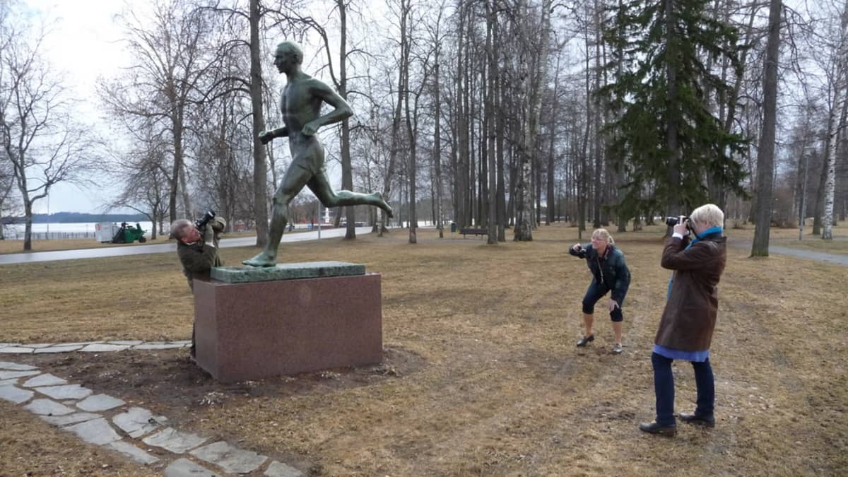 Kolme ihmistä hyörii kameran kanssa patsaan ympärillä.