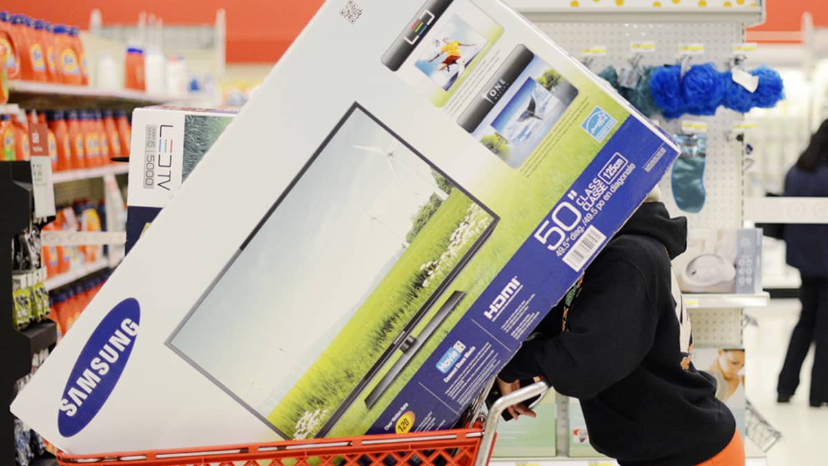 Nainenkuljettaa suurta televisiolaatikkoa ostoskärryissä.