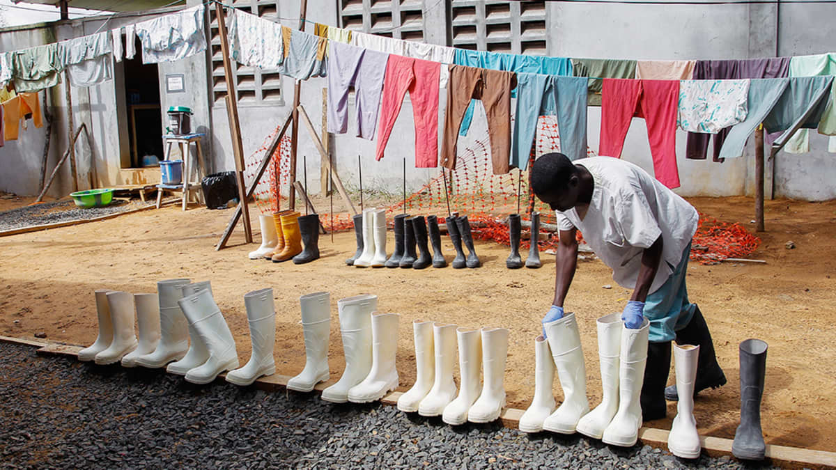 Liberialainen sairaanhoitaja desinfioi kumisaappaita Monroviassa.