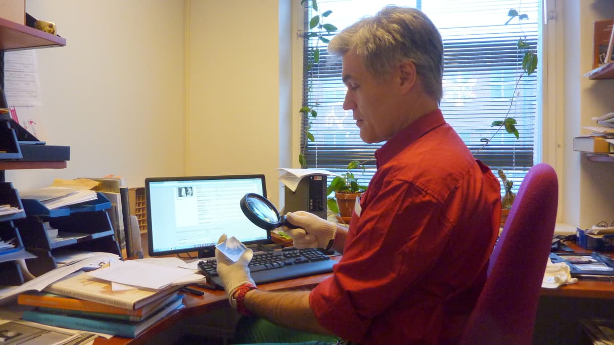 Tutkija Antti Liuttunen tarkastelee toimittajan mukanaan tuomaa vanhaa valokuvaa suurennuslasilla.