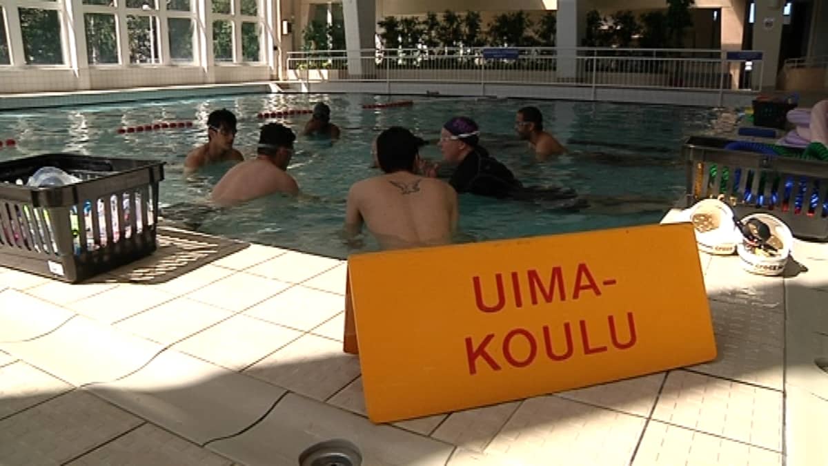 Maahanmuuttajia uimakoulussa. Uimakoulukyltti uima-altaan reunalla. 