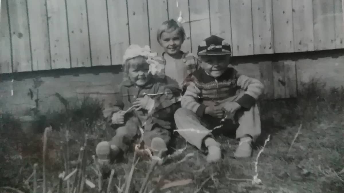 Kolme lasta istuu talon pihalla. 