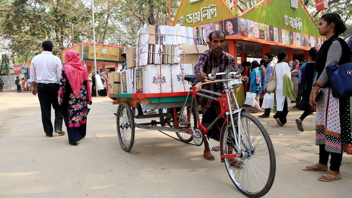 Mies kuljettaa kirjoja pyörällään Bangladeshin kirjamessuilla.
