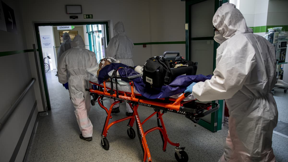 Suojapukuinen henkilökunta kuljettaa potilasta paareilla