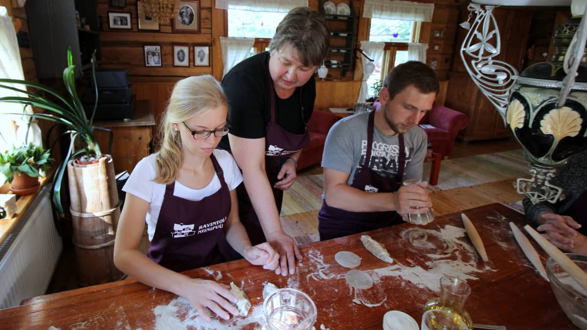 Paula Okkola neuvoo saksalaisturisteja karjalanpiirakoiden leipomisessa.