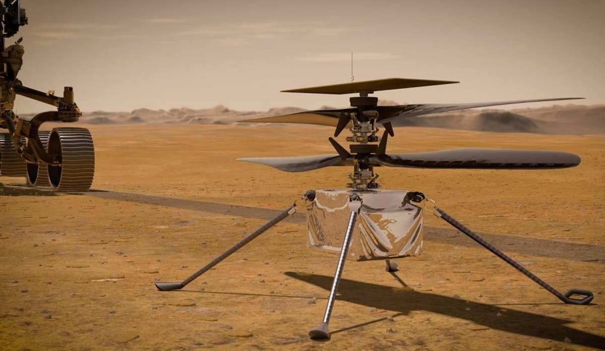 Neljällä pitkällä jalalla seisova laatikon muotoinen helikopteri Marsin punaisella pinnalla. Taustalla kuvasta rullaa pois mönkijä. 
