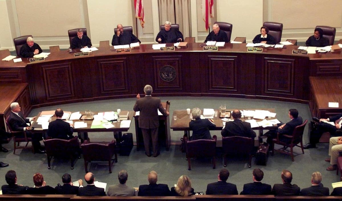 Laajassa kuvassa Floridan korkeimman oikeuden 6 tuomaria kuuntelee argumentoivaa miestä oikeussalissa. 