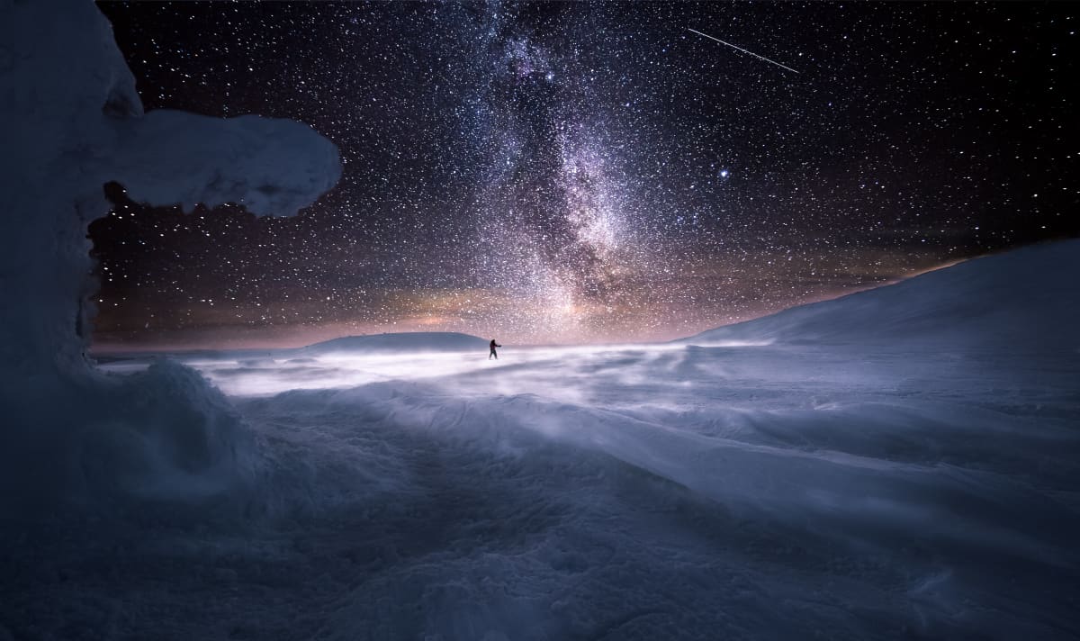 Hiihtäjä lumimaisemassa tähtitaivaan alla.