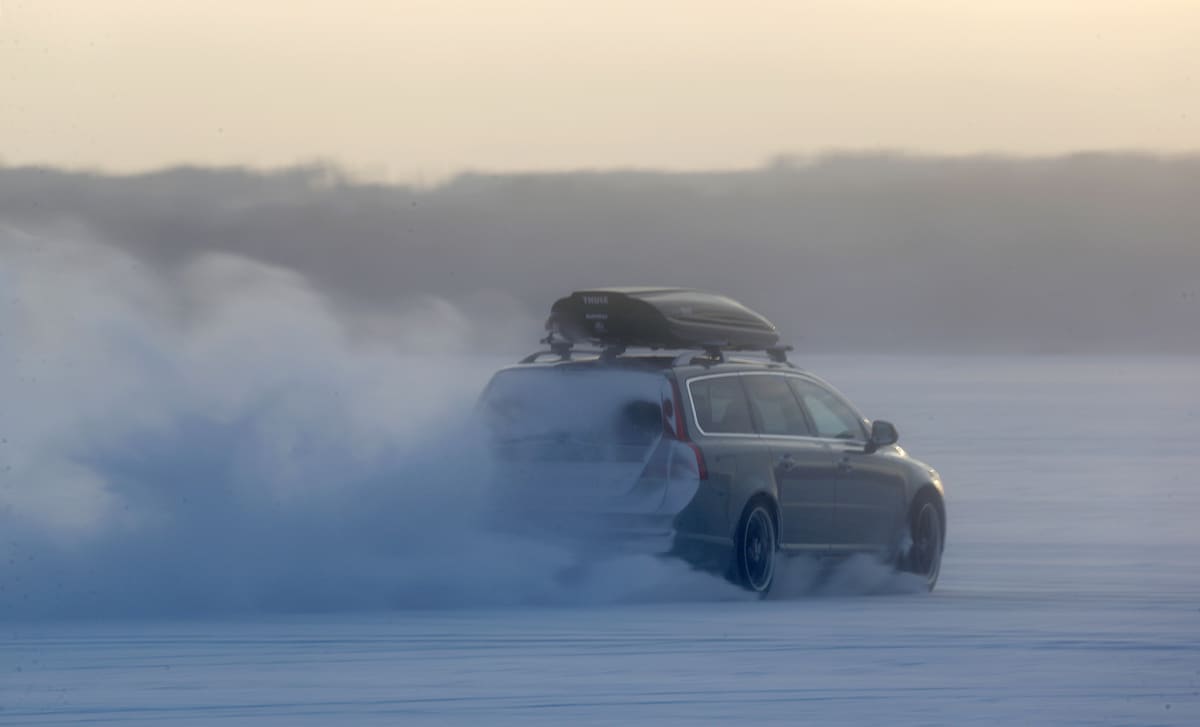 auto ajaa jäällä ja lumi pöllyää