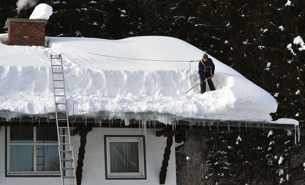 Mies pudottaa lunta katolta.