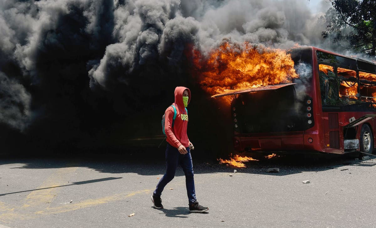 Mielenosoittaja kulkee palavan bussin ohitse Venezuelan Caracasissa.