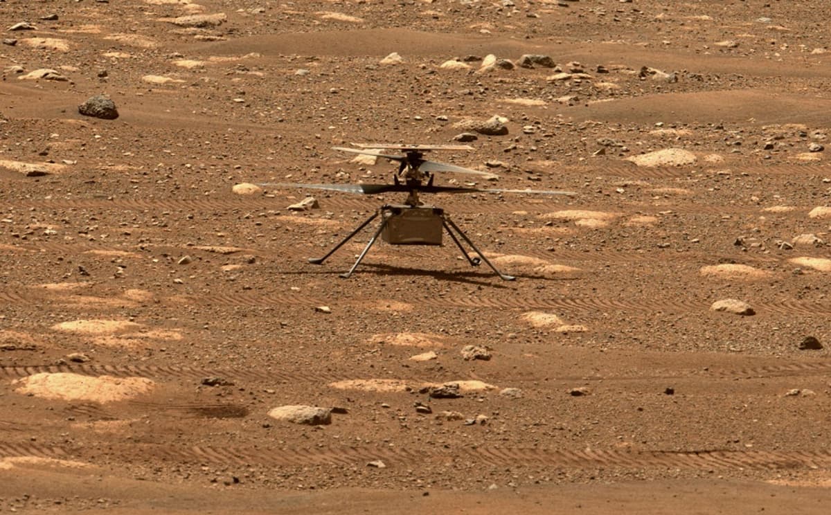 Laatikon muotoinen helikopteri seisoo neljällä ohuella jalalla Marsin kivisellä pinnalla. 