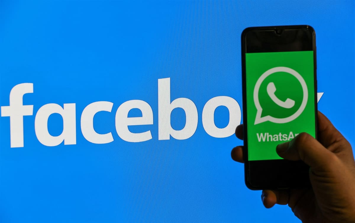 Kuvassa käsi pitelee kännykkää, jonka ruudulla nälyy Whatsapp-palvelun vihreä logo. Taustalla on Facebookin valkoinen teksti sinisellä pohjalla.