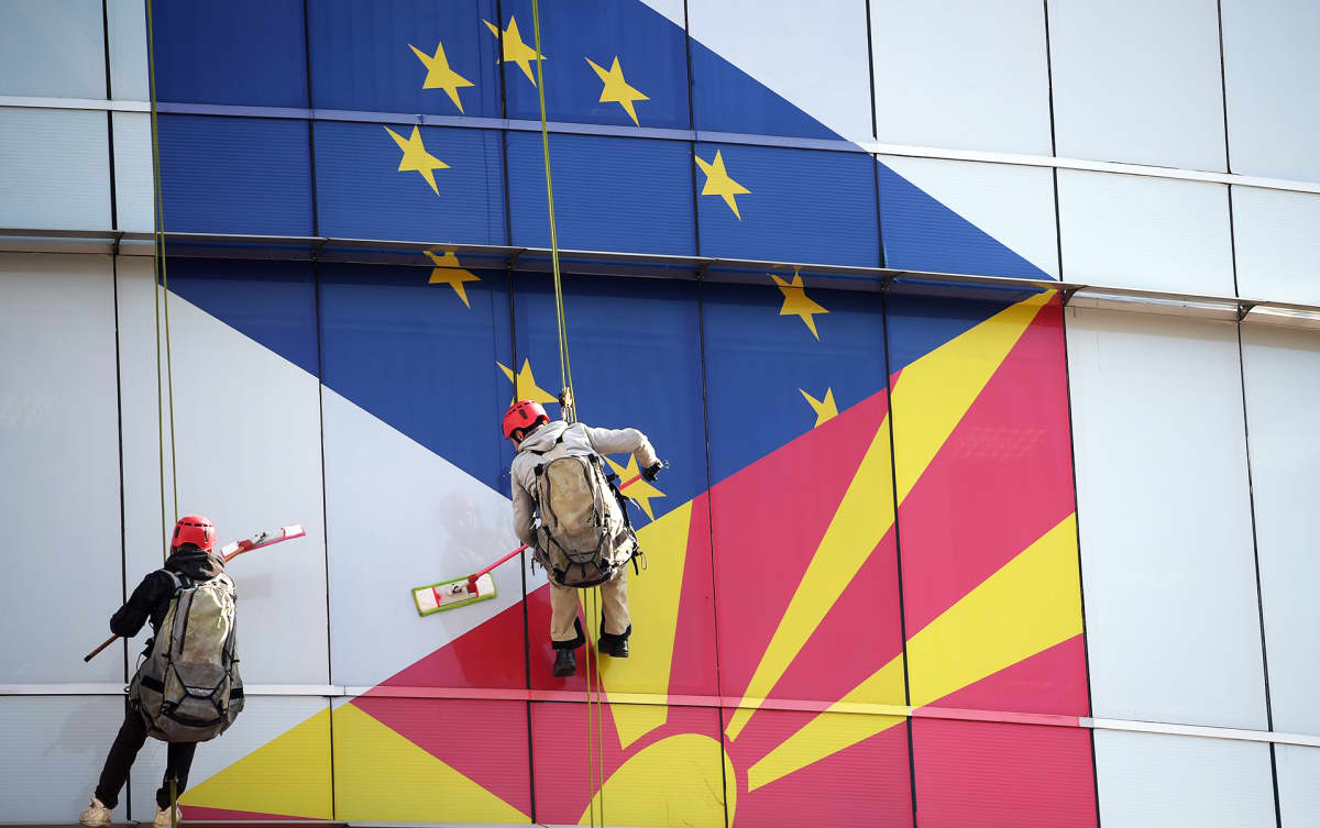 Työntekijät puhdistavat EU:n ja Pohjois-Makedonian lipuilla koristettua ikkunaa.
