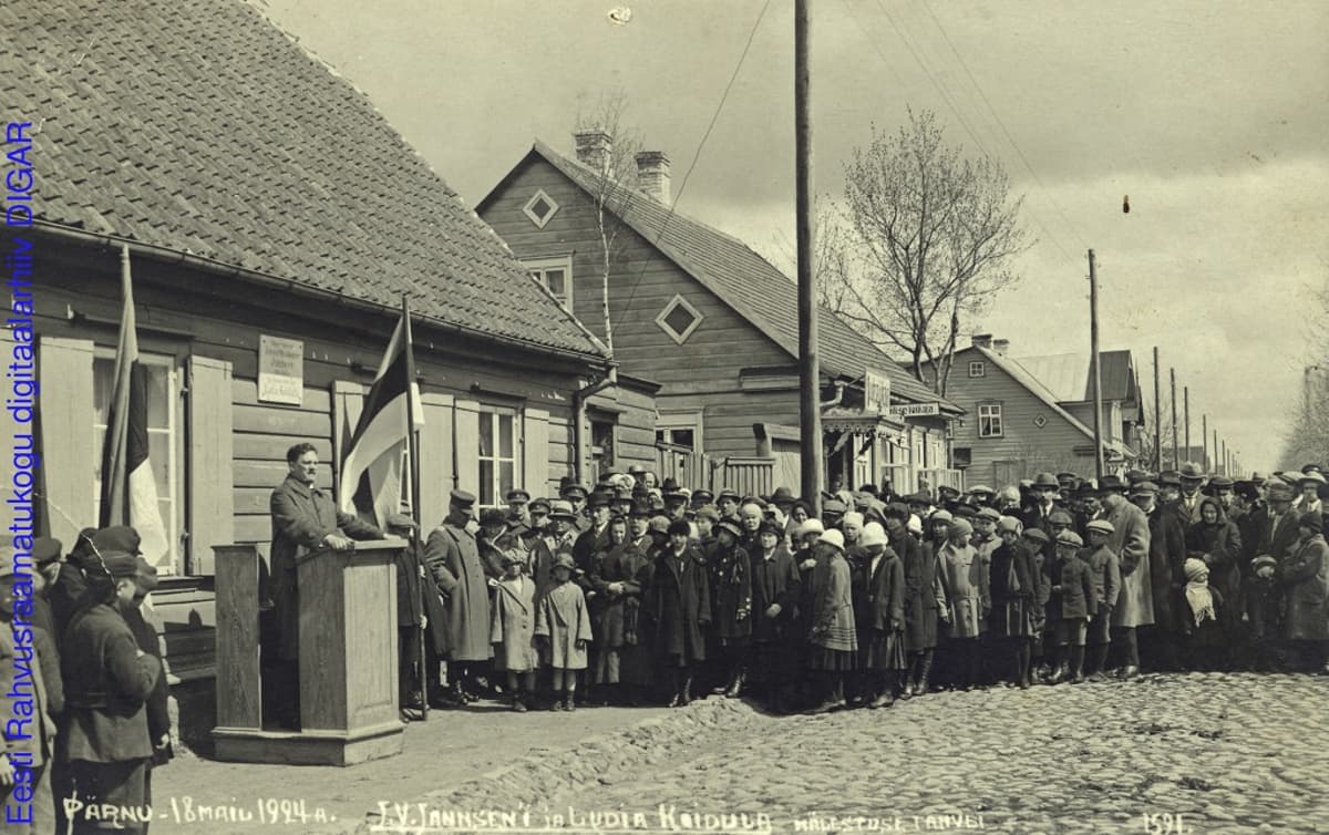 Mustavalkoinen valokuva väkijoukosta, joka seisoo kuuntelemassa puhujapöntössä olevaa miestä. Mukulakatu,puutaloja ja salossa Viron lippu.